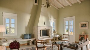 A spacious living room with a fireplace, comfortable seating, and large windows. - Villa Comi (Kefalonia)