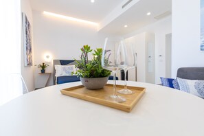 A modern living room with a round white table, a potted plant, and two wine glasses on a wooden tray. - Baia Flegrea Meublè - Deluxe Room (Bacoli)