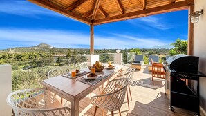 A wooden deck with a table and chairs, a grill, and a view of a hilly landscape. - Villa Carolina Private Pool (Agios Nikolaos)