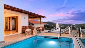 A pool area with a wooden deck, outdoor seating, and a view of the landscape. - Villa Carolina Private Pool (Agios Nikolaos)
