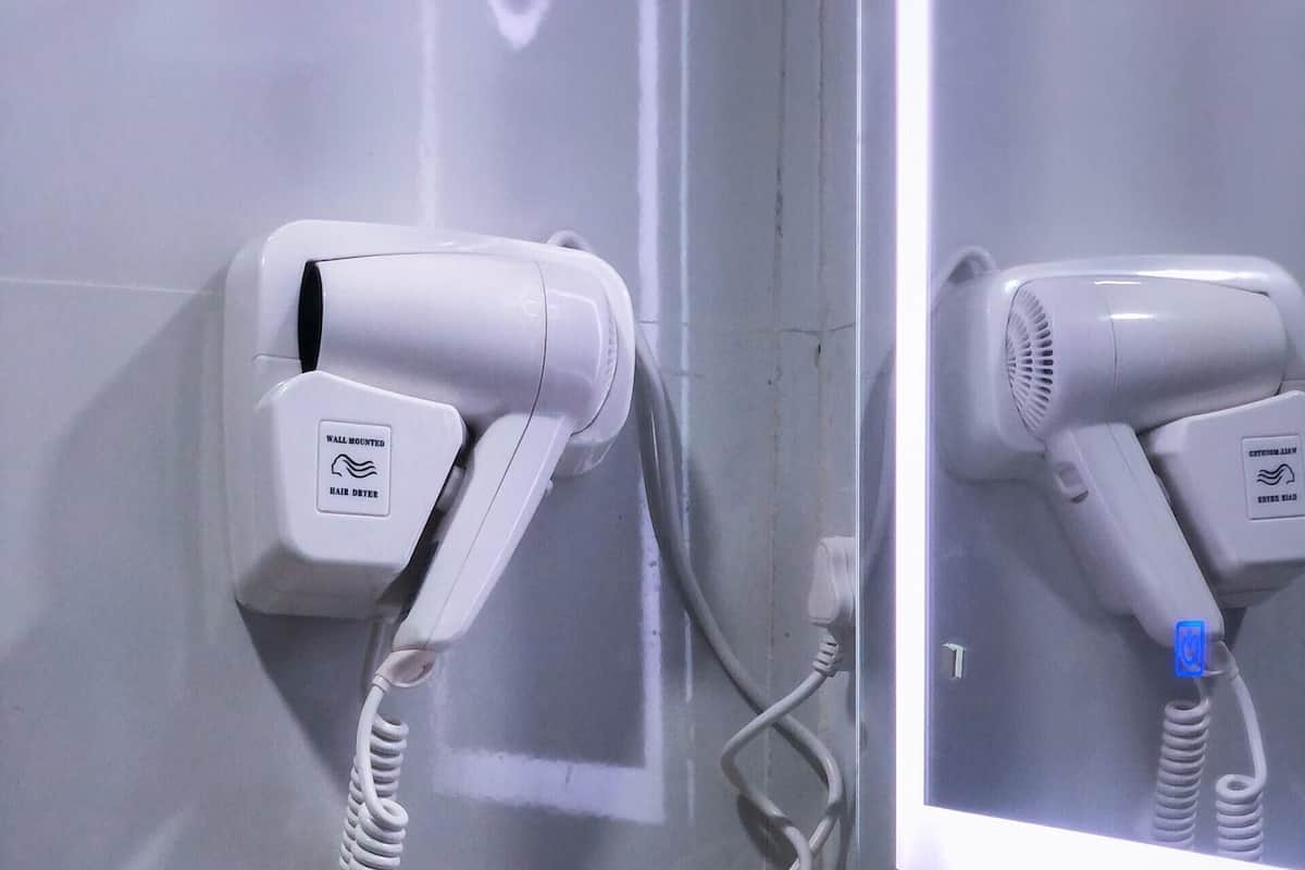 A bathroom with a hair dryer mounted on the wall, a mirror, and a yellow basket containing toiletries.