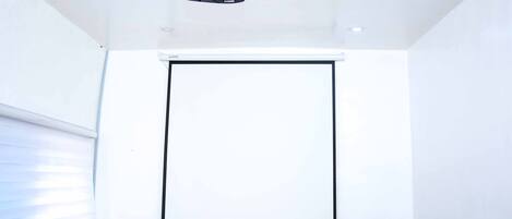 Un salón de conferencias con un proyector, una pantalla en blanco y dos sillas.