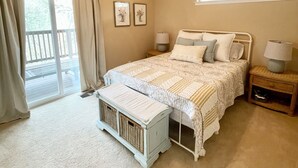 Un dormitorio con cama, ventilador de techo, mesita de noche, ventana con cortinas y vistas al exterior.