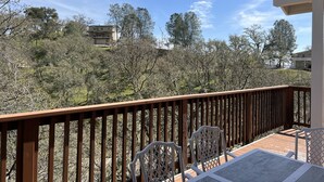 Una terraza de madera con una mesa y sillas, con vistas a un paisaje montañoso con árboles y edificios.