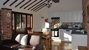 A cozy kitchen with white cabinets, a wooden dining table, and a built-in oven. - Hayloft Barn - Lodge Barns , Country Get Away, Morton near Southwell (Nottinghamshire)