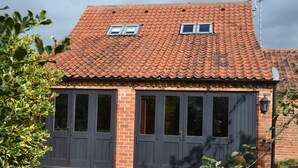 A two-story building with a red-tiled roof, two dark wooden doors, and a small window on the upper floor. - Hayloft Barn - Lodge Barns , Country Get Away, Morton near Southwell (Nottinghamshire)