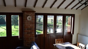 A room with a wooden ceiling, a brick fireplace, and large windows with a view of a garden. - Hayloft Barn - Lodge Barns , Country Get Away, Morton near Southwell (Nottinghamshire)