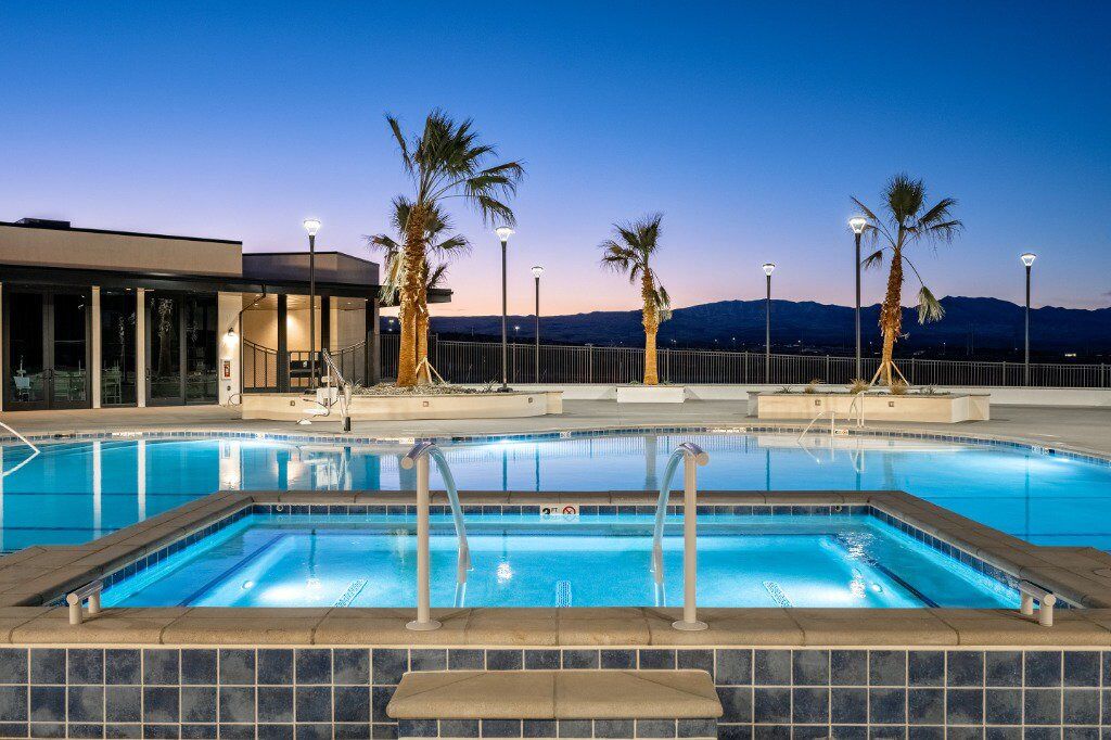 A swimming pool with a view of mountains, palm trees, and a building with glass doors.