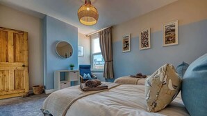 A bedroom with a bed, a wooden door, a round mirror, a bedside table, and a window with curtains. - 2-Bed Southsea House with Garden, Fireplace and Free Parking (Portsmouth)