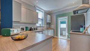 A modern kitchen with white cabinets, a built-in microwave, and a large window. - 2-Bed Southsea House with Garden, Fireplace and Free Parking (Portsmouth)