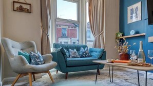 A living room with a sofa, armchair, and a table with decorative items. - 2-Bed Southsea House with Garden, Fireplace and Free Parking (Portsmouth)