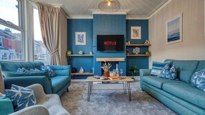 A living room with teal sofas, a coffee table, a TV, and artwork on the walls. - 2-Bed Southsea House with Garden, Fireplace and Free Parking (Portsmouth)