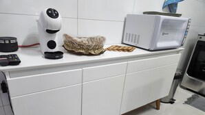 Eine Küche mit weißer Arbeitsplatte, einer Kaffeemaschine, einer Mikrowelle und einem Mülleimer.