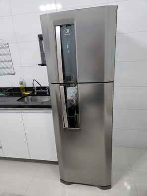 Un refrigerador de acero inoxidable con dispensador de agua, un fregadero y un escurreplatos en una cocina.
