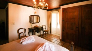 Ein Hotelzimmer mit einem großen Bett, zwei Stühlen, einem Schreibtisch, einem Spiegel und einer Holztür.