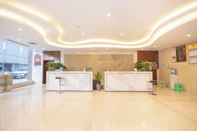 Zona de recepción de hotel con mostradores de mármol, un reloj de pared grande y una planta en maceta.