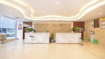 Zona de recepción de hotel con mostradores de mármol, un reloj de pared grande y una planta en maceta.