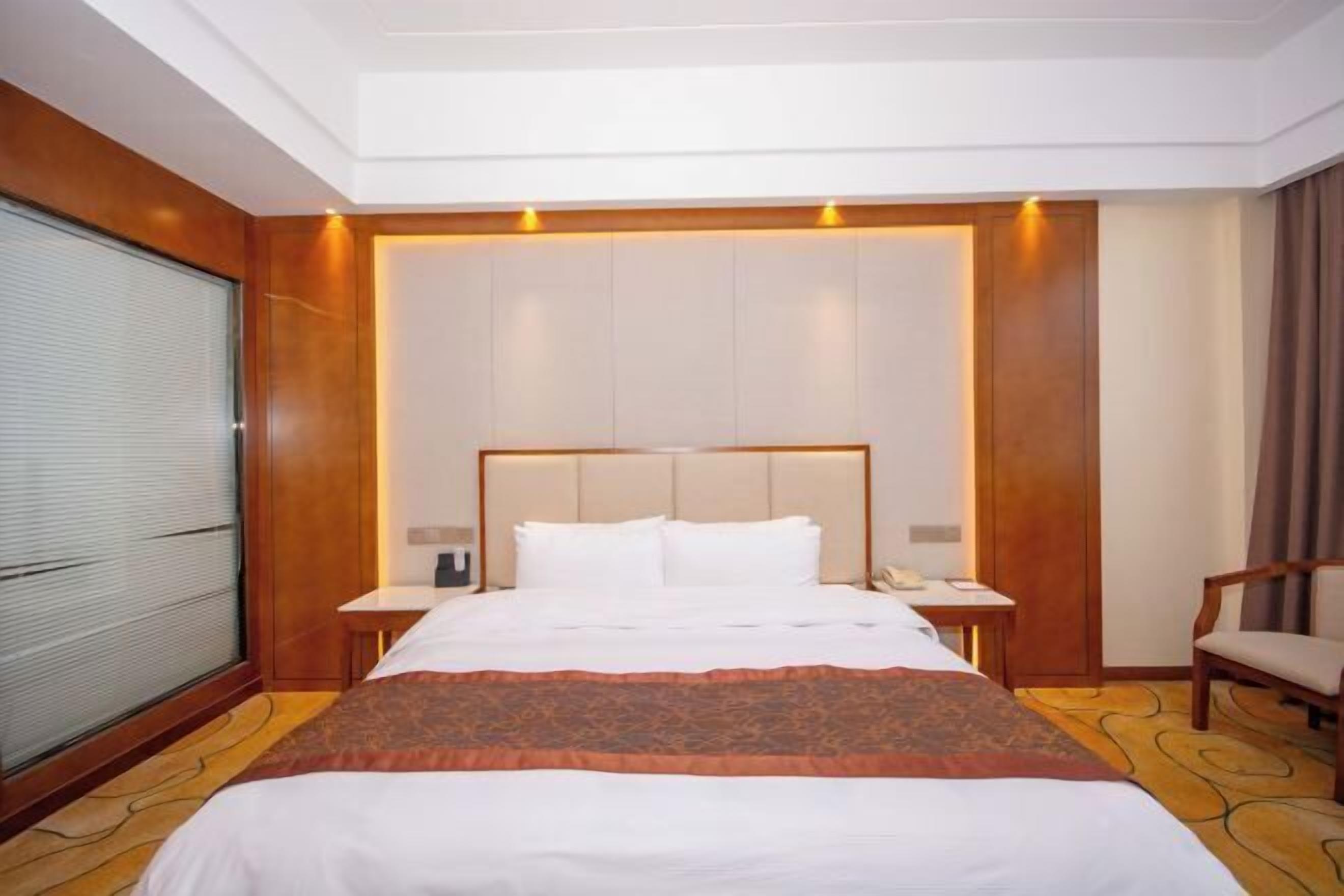 Une chambre d’hôtel avec un grand lit, une table de chevet, une chaise et une fenêtre avec des stores.
