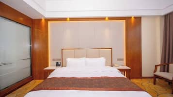 A hotel room with a large bed, a bedside table, a chair, and a window with blinds.