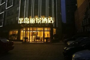 A hotel entrance with illuminated signage, a glass facade, and a paved driveway.