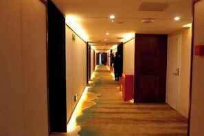 A hotel hallway with a carpeted floor, doors on the right, and a person walking in the distance. - Bandao Lijing Hotel (Lichuan)