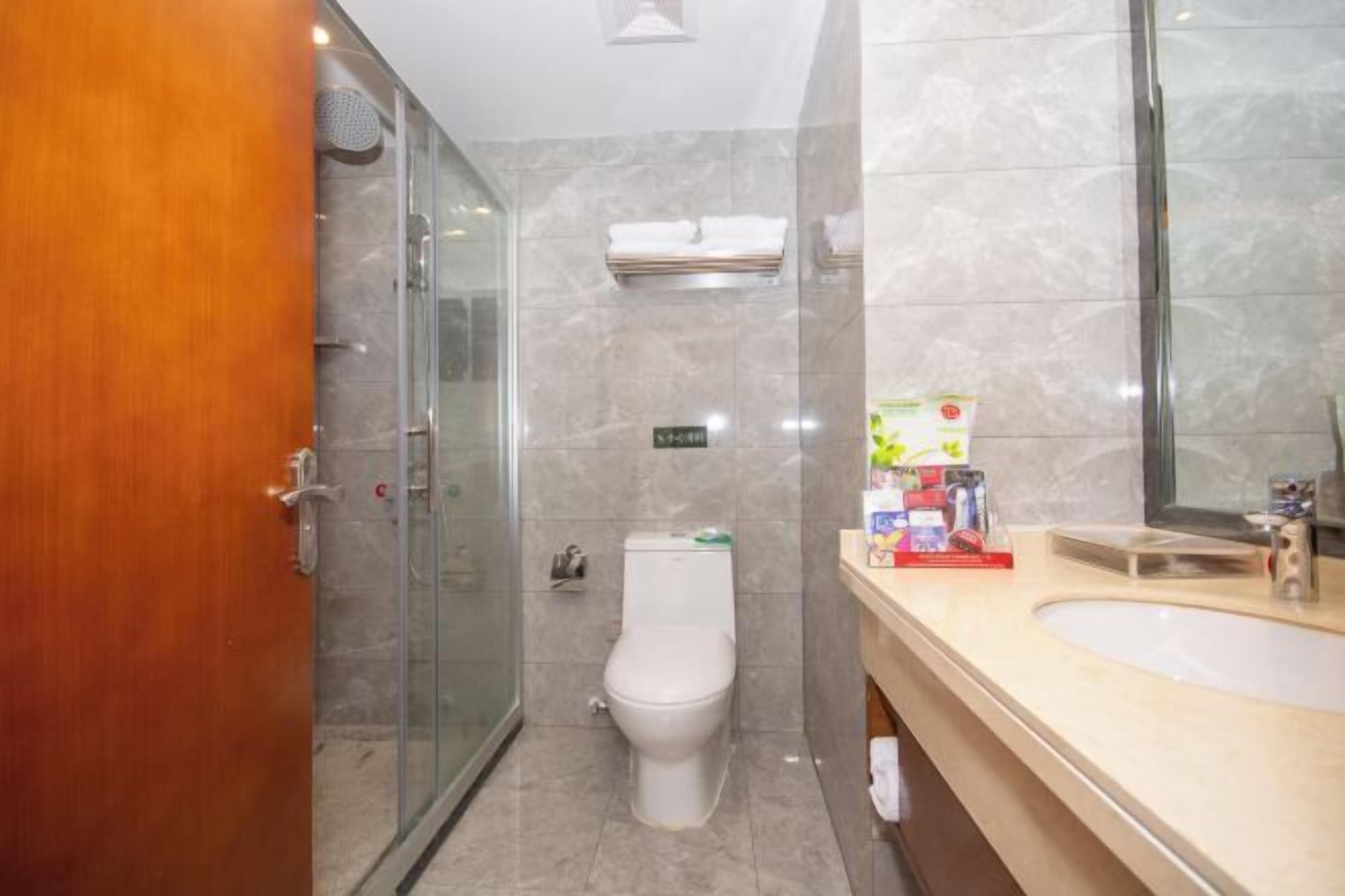 A bathroom with a glass shower enclosure, a toilet, a sink with toiletries, and a mirror.