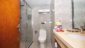 A bathroom with a glass shower enclosure, a toilet, a sink with toiletries, and a mirror.