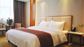 A hotel room with a large bed, a bedside table, a chair, and a small table with a plant.