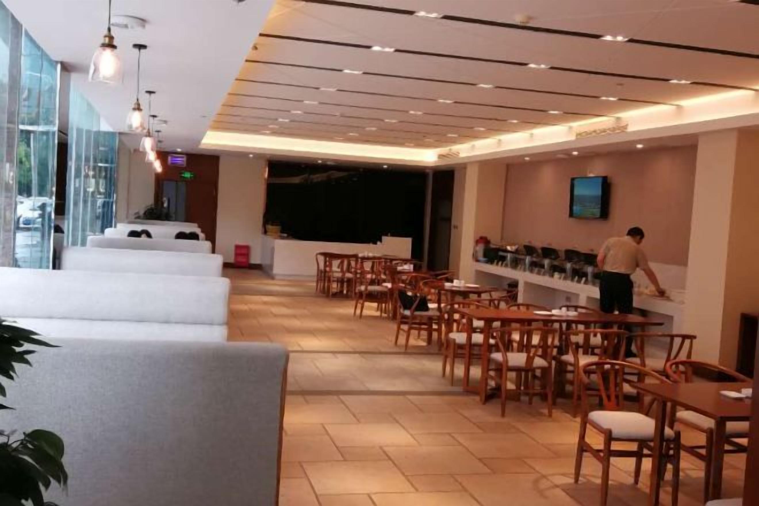 A modern restaurant with a bar area, seating arrangements, and a counter where a staff member is attending to customers.