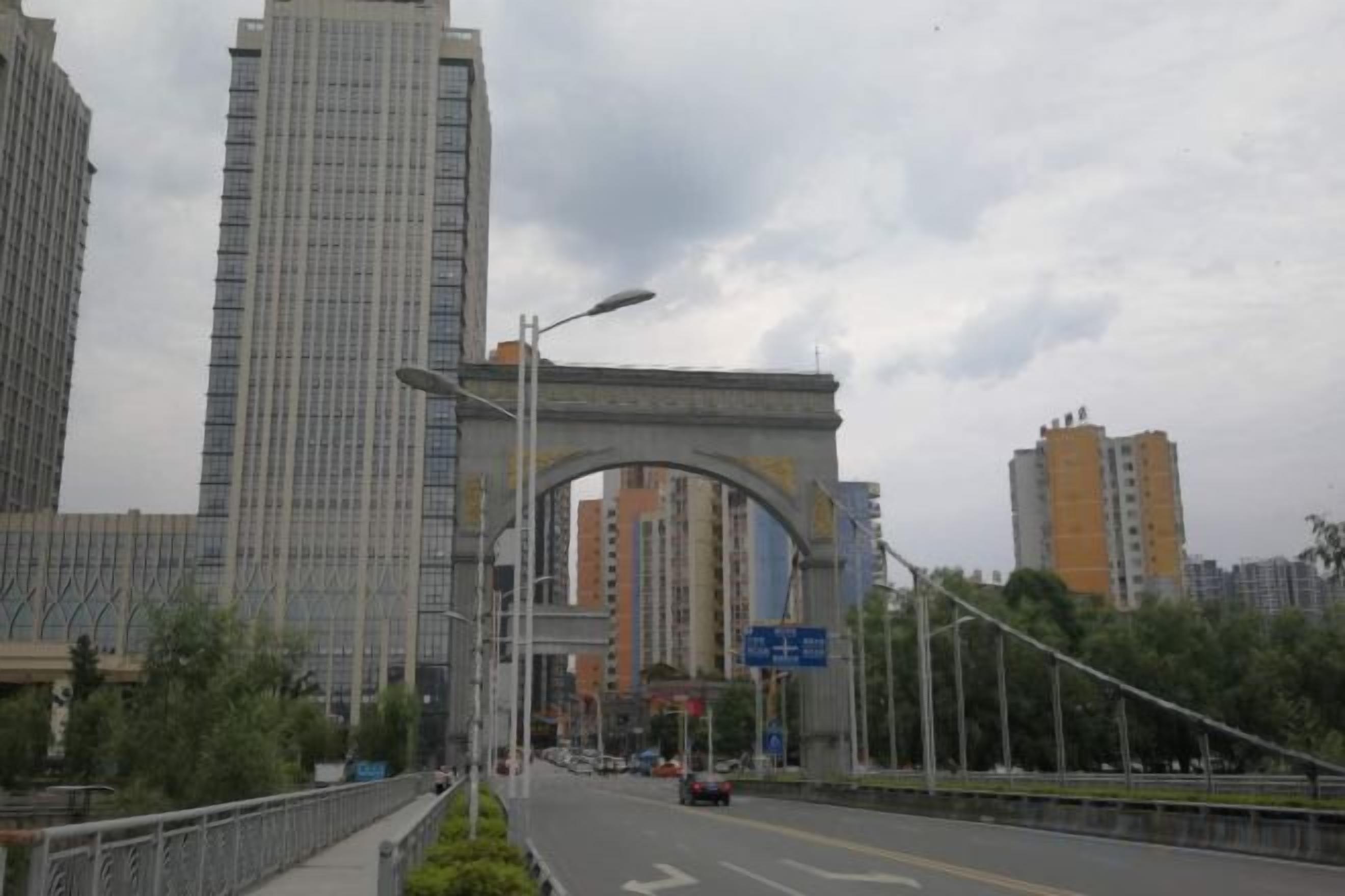Una calle urbana con un gran arco, edificios altos y cielo despejado.