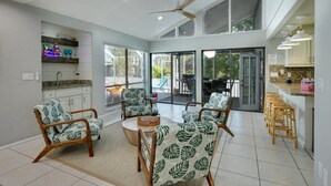 A spacious living area with a ceiling fan, large windows, and a kitchen area with bar stools.