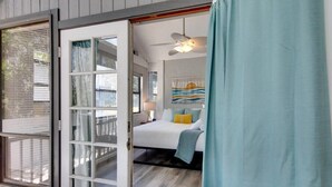 A bedroom with a bed, a ceiling fan, and a view of the outside.