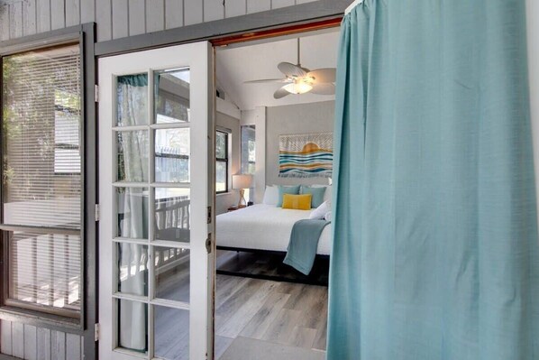 A bedroom with a bed, a ceiling fan, and a view of the outside.
