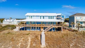 A coastal house with a large deck, multiple windows, and a staircase leading to the upper level. - Tuck Away - Stunning Ocean Front Designer Home (Atlantic Beach)