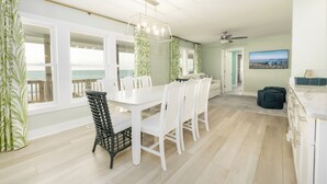 A dining area with a white table and chairs, large windows with curtains, a ceiling fan, and a view of the ocean. - Tuck Away - Stunning Ocean Front Designer Home (Atlantic Beach)