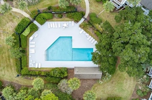 Vista aérea de una piscina rodeada de sillones blancos y un jardín cuidado.