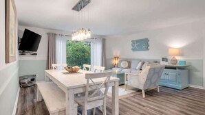 A dining area with a wooden table and chairs, a television mounted on the wall, and a view of greenery outside. - Relax & Enjoy Life! Updated Wild Dunes Condo (Isle of Palms)