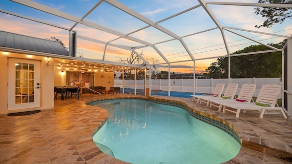 Une piscine intérieure avec un patio couvert, une table à manger et des chaises longues.