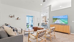 Ein modernes Wohnzimmer mit einem großen Flachbildfernseher, einer Couch, zwei Schaukelstühlen und einem Holzkasten.