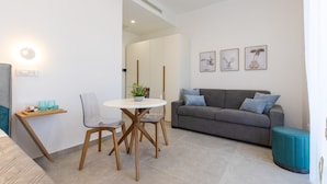 A modern living room with a grey sofa, a round white table, and two chairs. There are framed pictures on the wall and a small plant on the table.