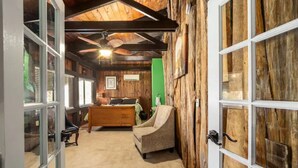 Une pièce chaleureuse avec un plafond en bois, un lit recouvert d’une couverture verte, une chaise et une fenêtre avec des stores.