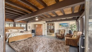 Un dormitorio amplio con una cama grande, techo de madera y vistas al área de estar.