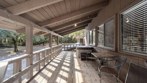 Une terrasse extérieure couverte, dotée d’un plancher en bois, de chaises en métal et d’une table.
