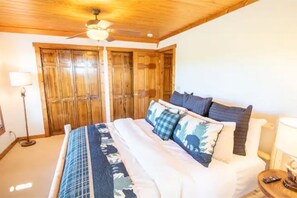 Een slaapkamer met een houten plafond, een bed met een gebedekt sprei en een nachtkastje met een lamp.