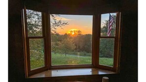 Una habitación con un amplio ventanal que da a un paisaje cubierto de hierba y un atardecer.