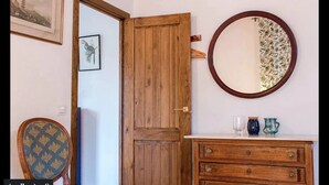 A room with a wooden door, a round mirror, a dresser, and a chair with a patterned cushion.