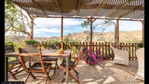 An outdoor patio with a table and chairs, a woven canopy, and a view of mountains.