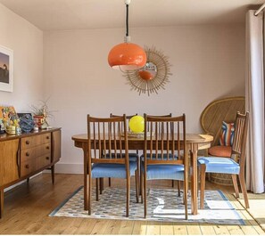 Un comedor con una mesa y sillas de madera, una lámpara colgante naranja y un adorno de pared.