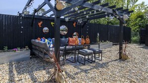 A covered outdoor seating area with a table and chairs, surrounded by a black fence and gravel ground. - 70s Inspired, 3-Bed Home in Rye with river views (Rye)
