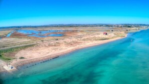 An aerial view of a coastal area with a clear blue water body, sandy shores, and sparse vegetation. - 70s Inspired, 3-Bed Home in Rye with river views (Rye)